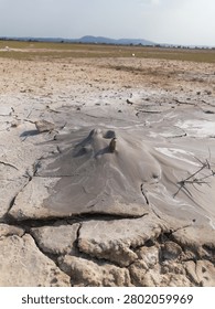 Active mud volcano erupting grey mud on a cracked arid landscape under a clear sky, Bledug Kuwu geological phenomenon
