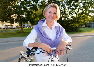 Active Old Age, Leisure And Lifestyle Concept - Portrait Of Senior Woman 60-65 Years Old On Bicycle. Older Lady Riding City Bike In Park. Old Smiling Female Cycling With Her Bike In Summer Time