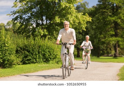 Active Old Age, People And Lifestyle Concept - Happy Senior Couple Riding Bicycles At Summer Park