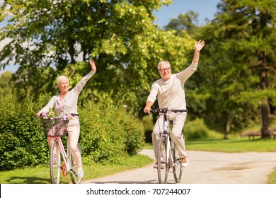active old age, people and lifestyle concept - happy senior couple riding bicycles and waving hand at summer park