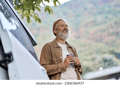 Active old happy hipster man standing near rv camper van on vacation. Mature traveler looking away enjoying view, holding drinking coffee waking up in the morning in camping tourism nature park. - Powered by Shutterstock