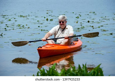 A Active Older Man Rows A Kayak On A Small Lake