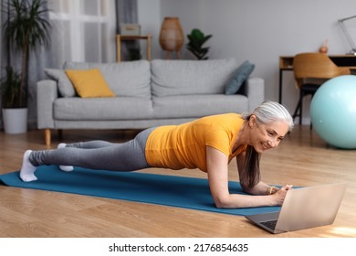 Active Older Woman Doing Exercises At Home, Watching Sport Videos Online On Laptop And Planking, Having Fitness Class, Copy Space. Healthy Lifestyle Concept