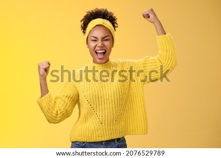 Active outgoing confident cheerful african-american female fan place bet hopefully yelling encourage team win standing raised fists victory celebrating gesture shouting proudly, yellow background