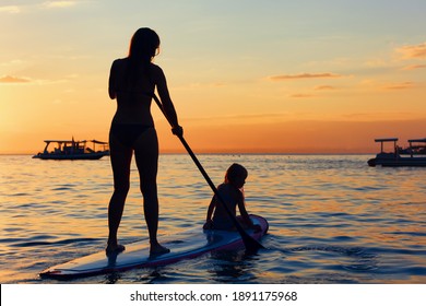 Active paddle boarder at sunset sea. Young mother with little clild paddling on stand up paddleboard. Healthy lifestyle. Water sport, SUP surfing tour in adventure camp on family summer beach vacation - Powered by Shutterstock