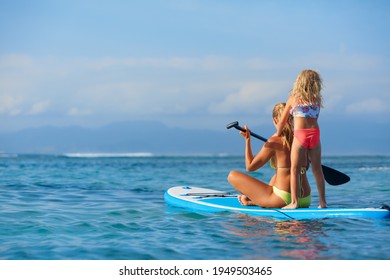 Active paddle boarder at sunset sea. Young mother with little clild paddling on stand up paddleboard. Healthy lifestyle. Water sport, SUP surfing tour in adventure camp on family summer beach vacation - Powered by Shutterstock