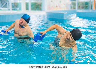 Active pensioners at a swimming pool doing aqua fitness exercises with the use of pool buoys. Swimming pool interior. Grandparents taking care of their health. High quality photo - Powered by Shutterstock