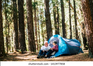 Active people old aged caucasian senior couple travel with camping tent - sit down in the forest having fun together - relationship forever concept for traveler wanderlust retired man and woman - Powered by Shutterstock