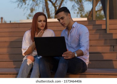 Active People. Photo Of Group Of Young Serious Bussines Couple Holding Laptop Computer Outside. Two Bussines People Using Laptop Outside Discussing Ideas With Colleagues.