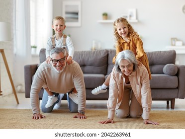 Active positive senior grandparents carrying excited little kids grandchildren on backs and smiling together at camera while playing and having fun in living room at home on weekend - Powered by Shutterstock