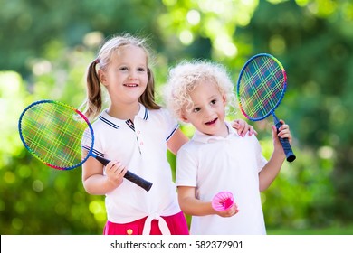 Active Preschool Girl And Boy Playing Badminton In Outdoor Court In Summer. Kids Play Tennis. School Sports For Children. Racquet And Shuttlecock Sport For Child Athlete. Kid With Racket And Shuttle