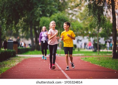 Active Recreation And Sports Children In Pre-adolescence. Caucasian Twins Boy And Girl 10 Years Old Jogging On Red Rubber Track Through Park. Children Brother And Sister Running On Treadmill Outside.