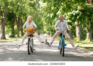 Active Retirement. Happy senior couple having fun while riding bicycles at summer park, cheerful mature man and woman cycling on retro bikes and laughing, enjoying outdoor leisure, copy space - Powered by Shutterstock