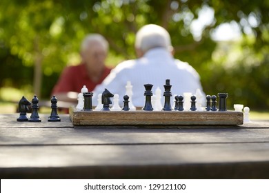 Active Retirement, Old Friends And Leisure, Two Senior Men Having Fun And Playing Chess Game At Park. Focus On Chessboard In Foreground