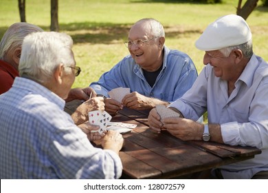 Active Retirement, Old People And Seniors Free Time, Group Of Four Elderly Men Having Fun And Playing Cards Game At Park. Waist Up
