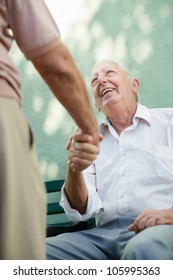 Active Retirement, Two Old Male Friends Talking And Shaking Hands On Bench In Public Park