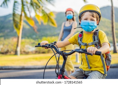 Active School Kid Boy And His Mom In Medical Mask And Safety Helmet Riding A Bike With Backpack On Sunny Day. Happy Child Biking On Way To School. You Need To Go To School In A Mask Because Of The