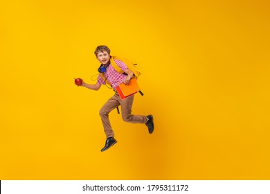 Active Schoolboy In Uniform With A Backpack, Books And An Apple Runs On A Yellow Background. Dynamic Images That Go Back To The Conceptual School. The Beginning Of Holidays. Boy Is Ready To Study.