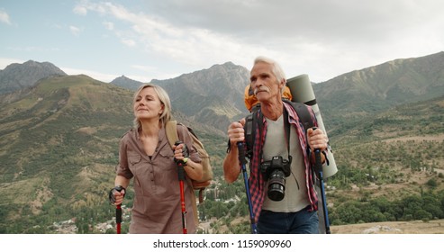 Active senior caucasian couple hiking in mountains with backpacks, enjoying their adventure 4k