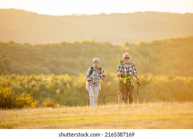 Active senior Caucasian couple hiking in mountains with backpacks and hiking poles, enjoying their adventure - Powered by Shutterstock