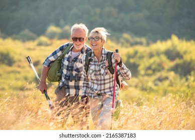 Active senior Caucasian couple hiking in mountains with backpacks and hiking poles, enjoying their adventure - Powered by Shutterstock