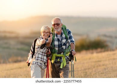 Active senior Caucasian couple hiking in mountains with backpacks and hiking poles, enjoying their adventure - Powered by Shutterstock