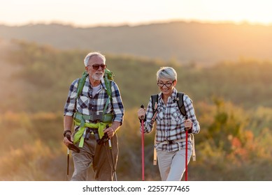 Active senior Caucasian couple hiking in mountains with backpacks and hiking poles, enjoying their adventure - Shutterstock ID 2255777465