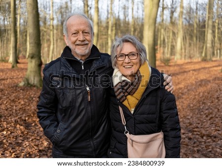 Active senior couple in an autumnal forest, walking and smiling; concept: pro-aging, healthy aging