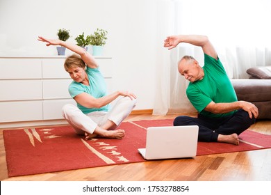 Active Senior Couple Doing Stretching Exercise And Watching Online Workout Tutorials On The Laptop In Living Room At Home.  Home Fitness, Activewear.