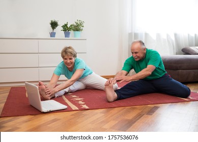 Active Senior Couple Doing Stretching Exercise And Watching Online Workout Tutorials On The Laptop In Living Room At Home.  Home Fitness, Activewear.