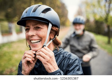 Active senior couple with electrobikes standing outdoors on a road in nature.
