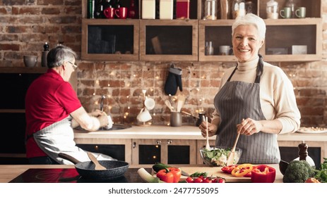 Active senior couple enjoys cooking together in their kitchen. The man is washing dishes while the woman mixes a salad. They both look happy and relaxed, enjoying each others company. - Powered by Shutterstock