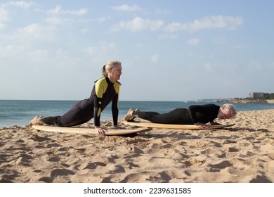 Active senior couple exercising on surfboards on shore. Sporty man and woman lying on big boards and practicing positions before riding on waves. Sport and healthy lifestyle for aged people concept - Powered by Shutterstock