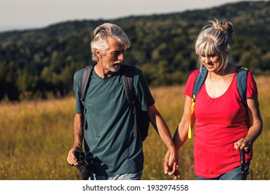 Active Senior Couple Hiking In Nature With Backpacks, Enjoying Their Adventure At Sunset.