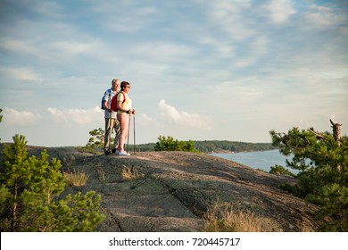 Active Senior Couple Hiking On The Top Of Rock, Exploring. Mature Man And Woman Happily Smiling. Nordic Walking, Trekking. Scenic View Of Gulf And Sea. Healthy Lifestyle. Finland.