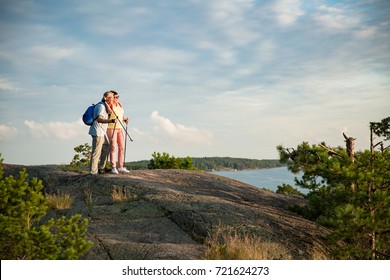 Active senior couple hiking on the top of rock, exploring. Mature man and woman Happily smiling. Nordic walking, trekking. Scenic view of gulf and sea. Healthy lifestyle. Finland. - Powered by Shutterstock