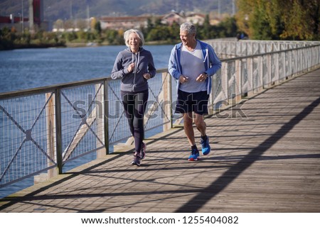  Active senior couple jogging together on bridge                              