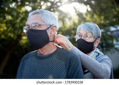 Active Senior Couple On Outdoor Walk Wearing Face Masks. Woman Helping Man With Mask.