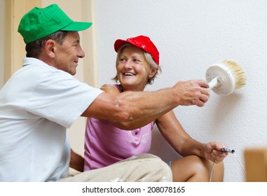 Active Senior Couple Painting Wall With Brush In New House. They Are Having Fun.