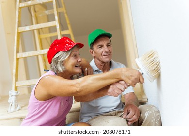 Active Senior Couple Painting Wall With Brush In New House. They Are Having Fun.