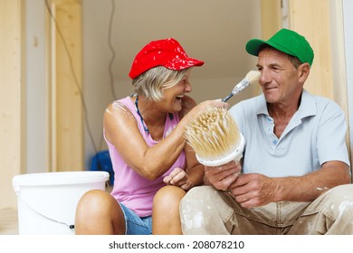 Active Senior Couple Painting Wall With Brush In New House. They Are Having Fun.