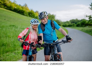 Active senior couple resting after bicycle ride at summer park, using smartphone. - Powered by Shutterstock