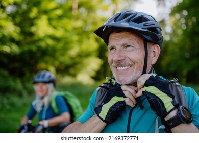 Active senior couple riding bicycles at summer park, man is putting on helmet, healthy lifestyle concept. - Powered by Shutterstock