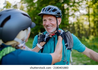 Active senior couple riding bicycles at summer park, man is putting on helmet, healthy lifestyle concept. - Powered by Shutterstock