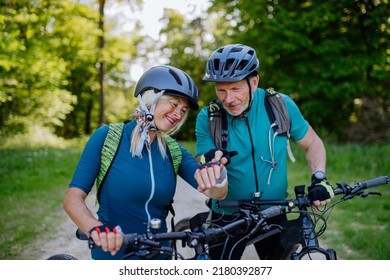 Active senior couple riding electric bicycles on road at summer park, checking their performance at smartwatch, healthy lifestyle concept. - Powered by Shutterstock