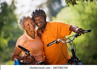 Active Senior Couple Standing With Bicycles In Park, Cheek To Cheek, Smiling, Portrait (tilt)