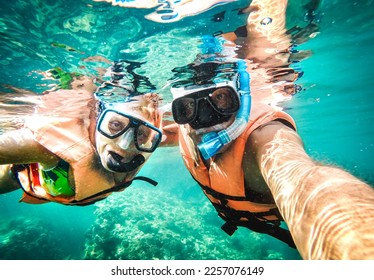 Active senior couple taking under water selfie in tropical sea excursion with water camera - Boat trip snorkeling in exotic scenario - Retired elderly life style concept on scuba diving - Vivid filter - Powered by Shutterstock