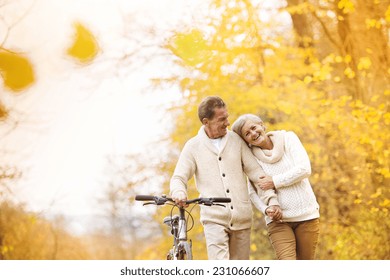 Active senior couple together enjoying romantic walk with bicycle in golden autumn park - Powered by Shutterstock