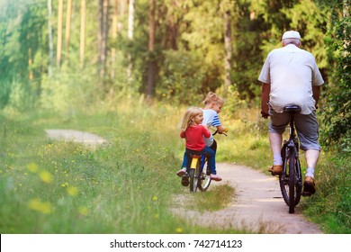 Active Senior With Grandkids Riding Bikes In Nature