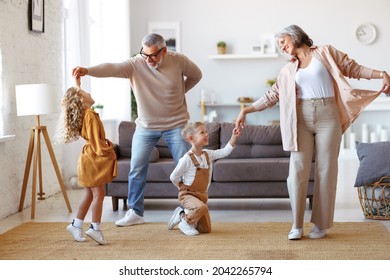 Active senior grandparents dancing with two happy kids grandchildren in living room, small children sister and brother having fun in living room while playing with grand mother and grandfather